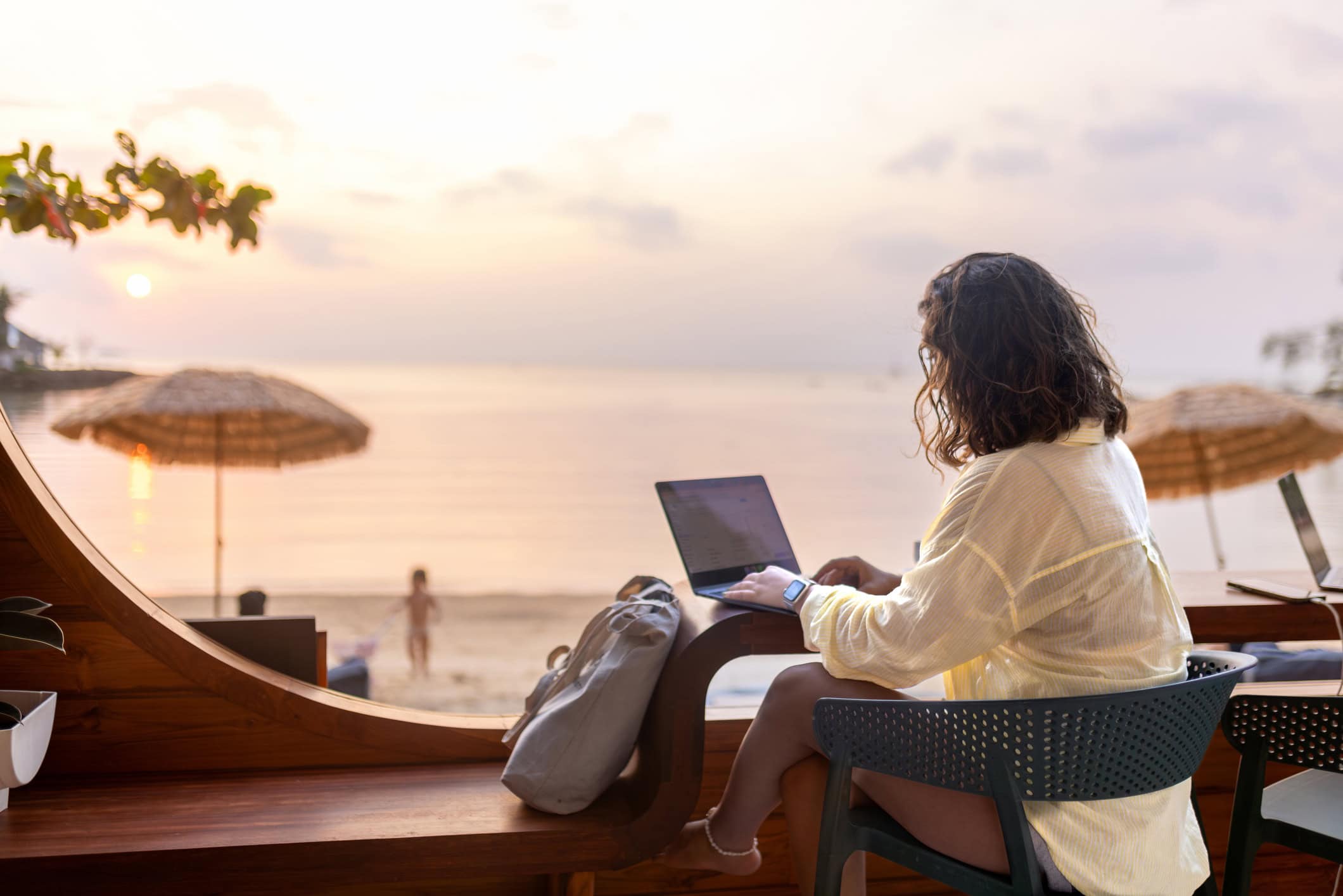 Woman with curly hair using a laptop on a beach at sunset.
